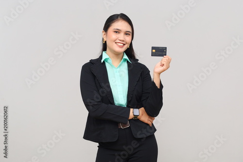 A beautiful young Asian business woman wearing a suit, smiling, showing a credit card for online payment, isolated on a white background.