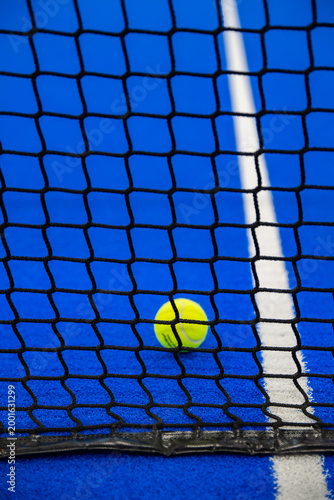 Tennis ball behind a black net on a bright blue padel court with white boundary line