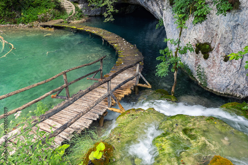Canvastavla Wooden boardwalk curves turquoise lake enter cave rocky cliff covered moss greenery