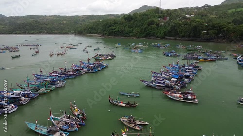 Aerial drone view of numerous traditional fishing boats anchored in a scenic tropical bay surrounded by lush green hills.