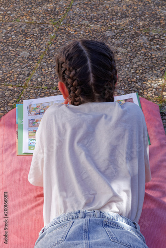 Bild auf Leinwand Jeune fille vue de dos lisant une BD couchée sur un  matelas