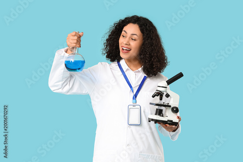 Female African-American scientist with microscope and flask on blue background