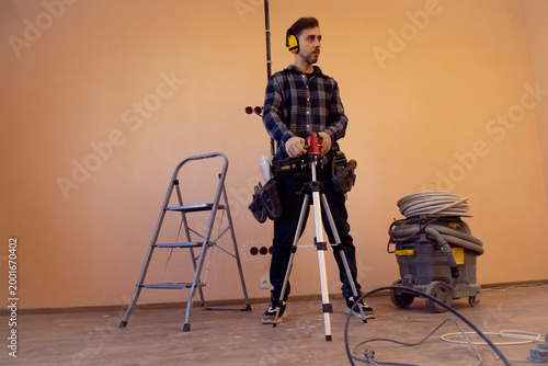 Repair specialist uses laser level to mark lines for future electrical wiring installation in indoor construction space