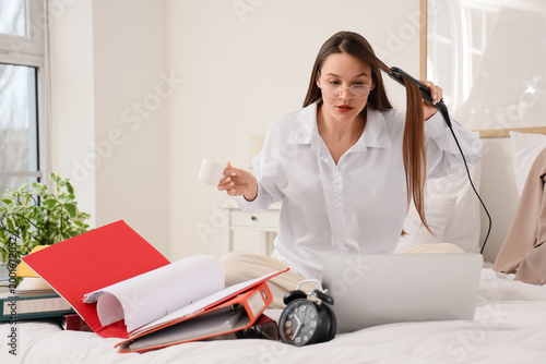 Hurrying young woman straightening hair and drinking coffee in bedroom