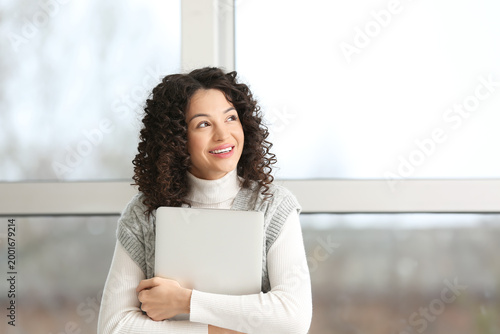 Fotografie Young businesswoman with laptop looking upwards near window in office