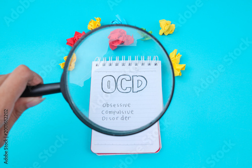 Hand Holding Magnifying Glass Over Notepad With OCD Text And Crumpled Papers For Mental Health Concept