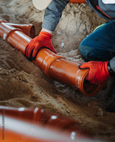 Close-up of worker joining PVC sewer pipes in sand trench. Underground drainage installation with focus on pipe connection and alignment.
