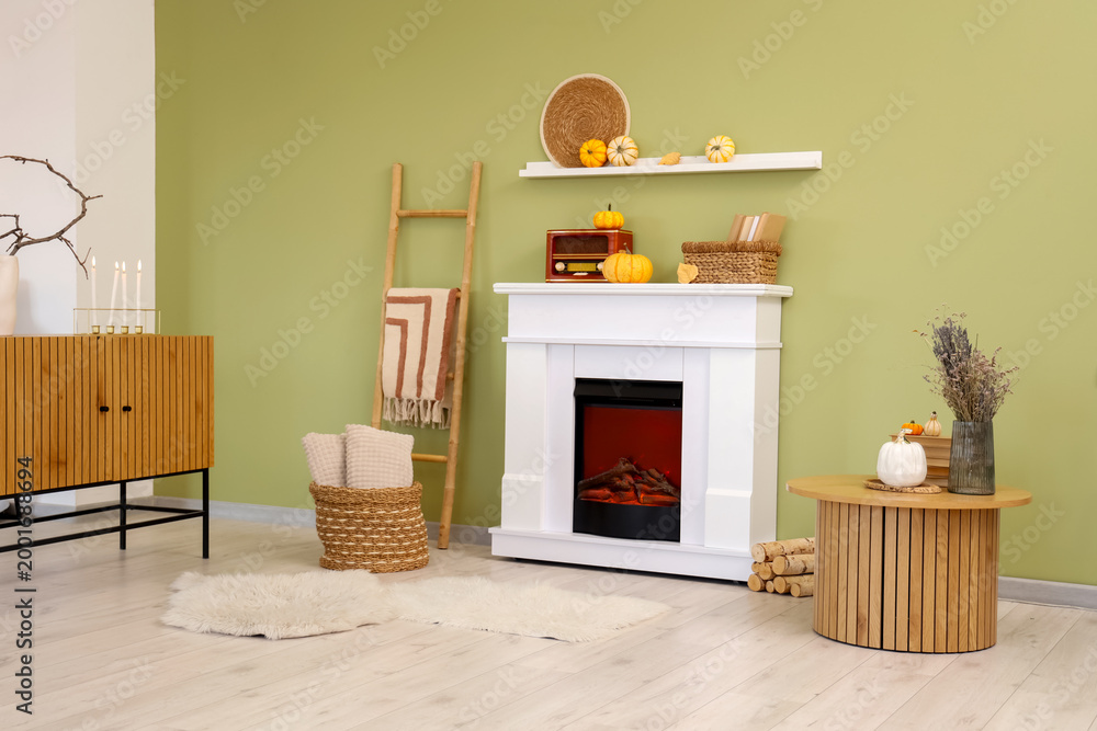 Naklejka premium Interior of stylish room with table, vintage radio receiver and pumpkins on modern fireplace near green wall