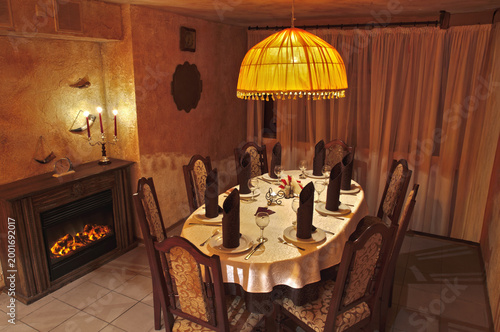 Stylish interior of an empty modern cafe with wooden furniture and chandelier Elegant evening restaurant setting with fireplace and private dining table