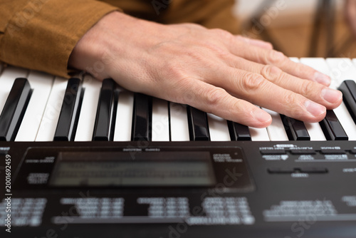 Closeup photo of young man playing synthesizer at home. Casual home piano session, hand resting on keyboard keys.