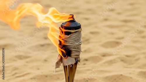 Burning torch with flame on sandy beach background  