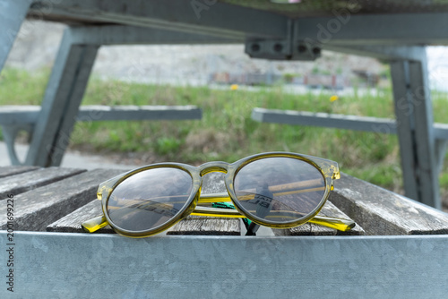 Modern yellow transparent sunglasses resting on a wooden picnic table outdoors