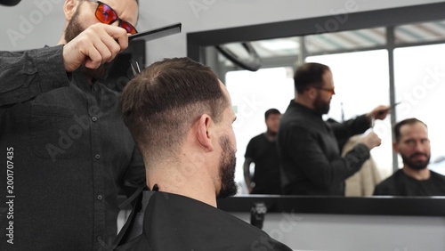 Obraz na płótnie Skilled barber working on male client's hairstyle, carefully combing and prepari