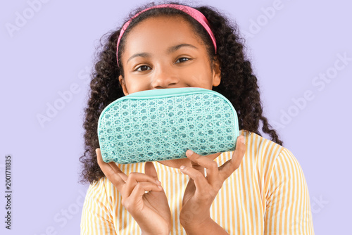 Little African-American girl with pencil case on lilac background