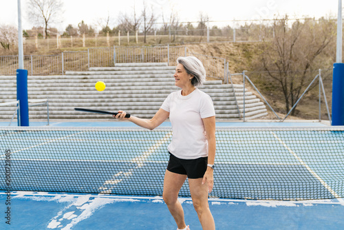 Canvastavla Senior woman enjoying pickleball, hitting the yellow ball with a paddle, staying