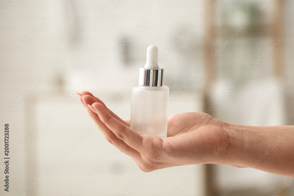Naklejka premium Female hand holding bottle of cosmetic product in bathroom, closeup