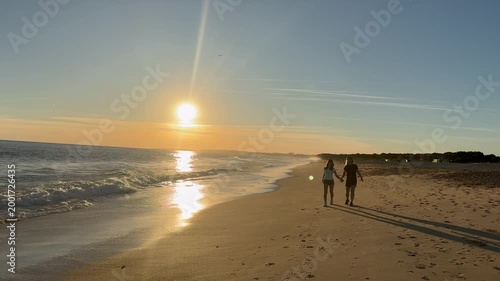 mother and daughter walking along the beach at sun