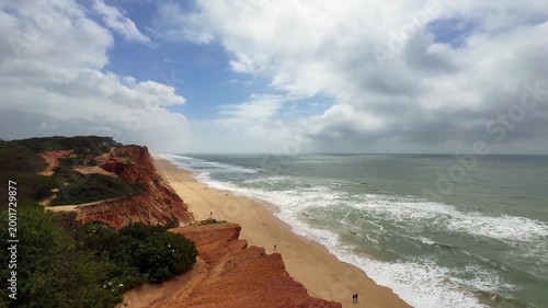 Landscape view of the Algarve coast, red cliffs, several pine trees on the upper part of the cliffs, beautiful blue sky