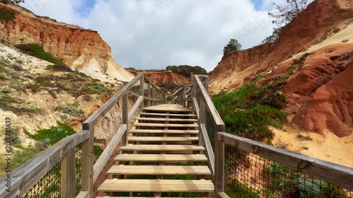 Scenic view of cliffs in Portugal with ocean waves and a wooden pathway leading through the rugged landscape.
