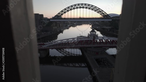 Aerial predawn view through a foreground frame toward the River Tyne in Newcastle, featuring the Swing Bridge and Tyne Bridge with the Millennium Bridge and The Glasshouse in the distant background.