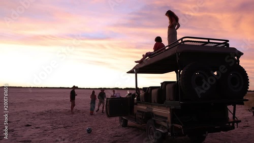 brother and sister atop safari vehicle looking at sunset, Makgadigadi National Park, Botswana, Africa