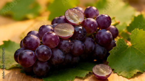 Close-up of ripe purple grapes on green leaves with sliced halves revealing translucent flesh. Warm golden lighting highlights the organic texture and fresh harvest mood.