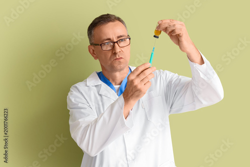 Mature doctor with ampule and syringe on green background