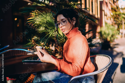 Bild auf Leinwand Confident multiracial woman holding smartphone and stylus at outdoor terrace, digital nomad checking notifications, mobile banking and online shopping concept, modern business communication