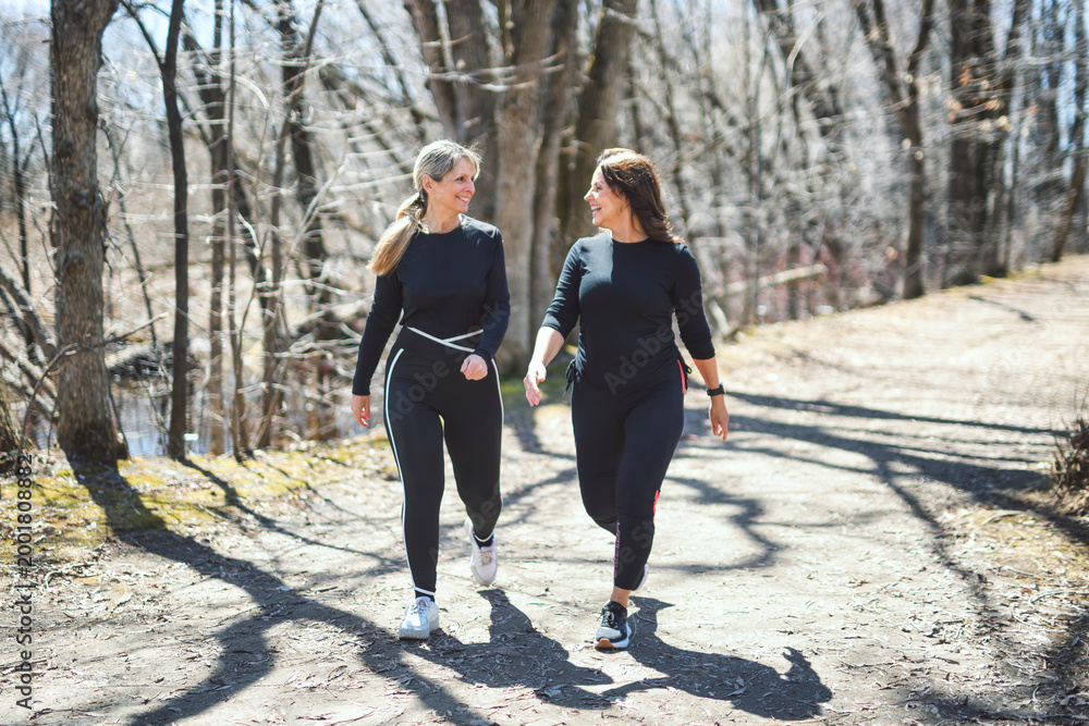 Fototapeta premium Energetic middle-aged woman jogs through a tree-lined path
