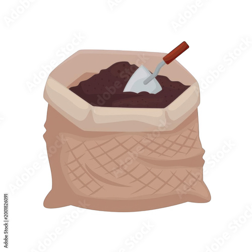 A bag of soil with a shovel on top sits outdoors.