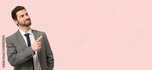 Handsome businessman pointing at something on pink background with space for ...