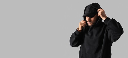 Young man in black hoodie and with baseball cap on grey background with space for text