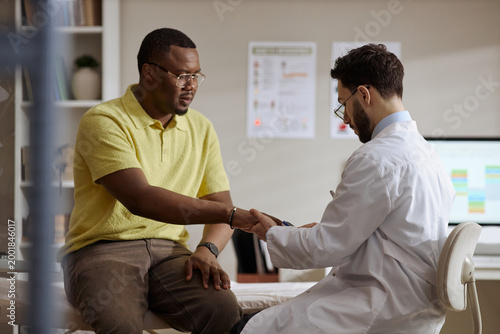 Εκτύπωση καμβά African American young adult man extending hand to male doctor during medical consultation, discussing symptoms and trust