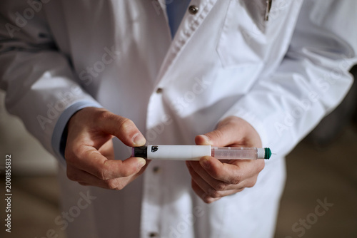 Close up of middle aged doctor holding prefilled insulin injection pen, demonstrating medical treatment process. Useful for healthcare marketing, diabetes care, vaccination content