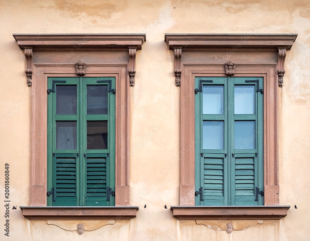 Fototapeta premium Two rectangular windows with green shutters and stone frames on a peach-colored wall