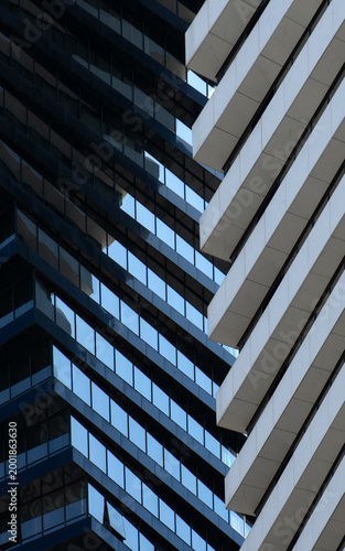 A tight, close-up abstract of two modern building facades meeting in a geometric composition. The shot focuses on the rhythmic contrast between the dark blue glass window grid and the sharp