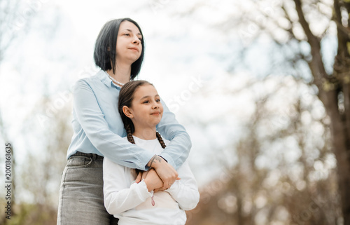 Loving mother hugging her little daughter in the park while looking away together at the view