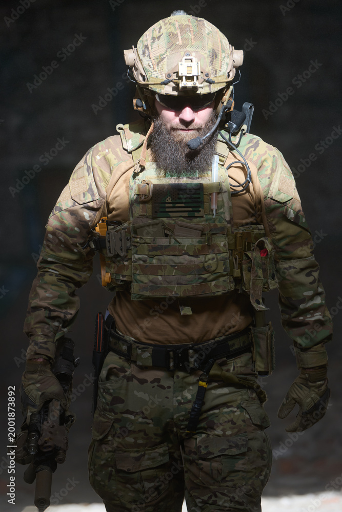 Fototapeta premium Bearded Soldier Wearing Camouflage Tactical Gear And Helmet Holding Rifle During Urban Operation