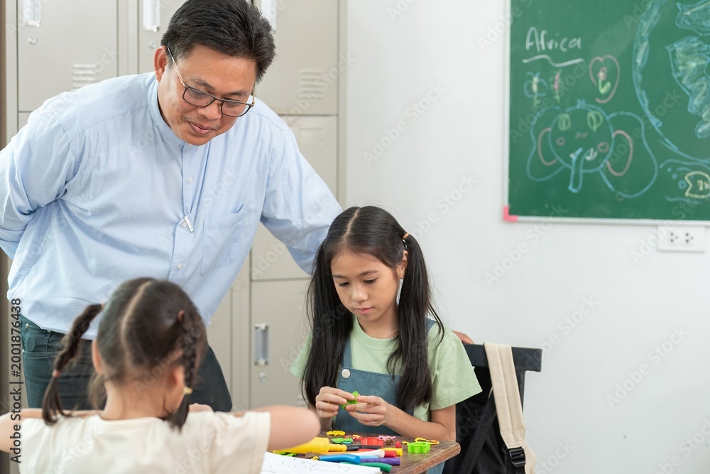 Obraz premium Teacher guiding children drawing and playing with modeling clay in art class creative learning activity at school. Male Instructor teaching primary students using colorful materials in classroom.