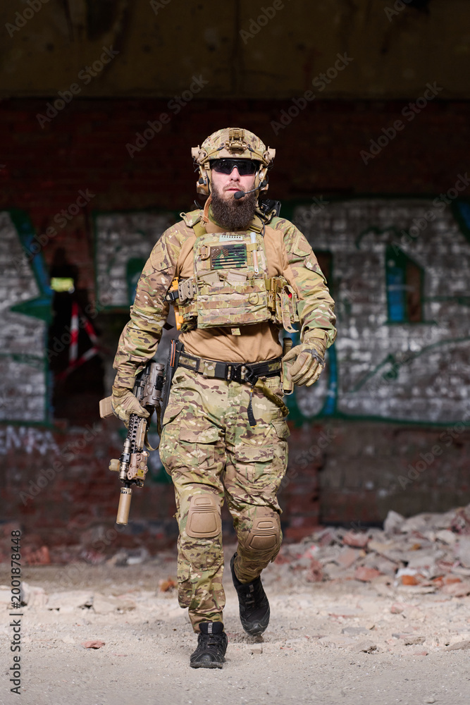 Fototapeta premium Armed Soldier in Tactical Gear Walking Through Urban Ruins With Rifle and Helmet