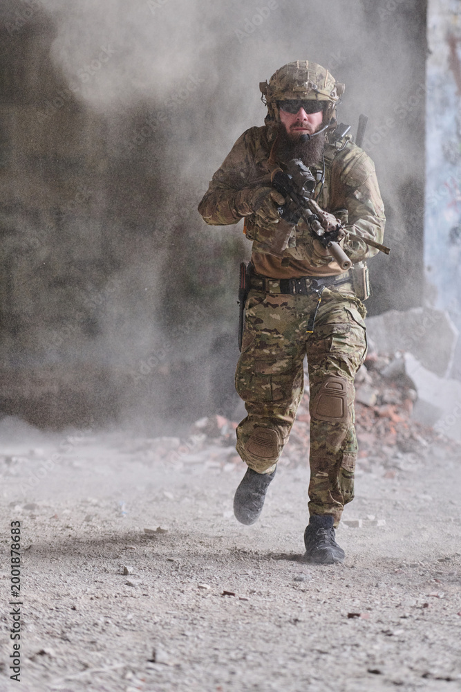 Fototapeta premium Armed Soldier In Camouflage Running With Rifle During Urban Combat Training In Dusty Ruins