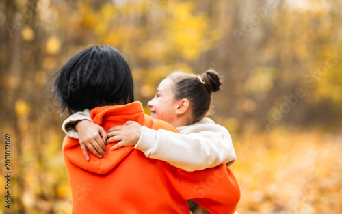 Close up of mother embracing her little daughter among falling autumn leaves, authentic family bonding, sincere love and warmth in fall park	