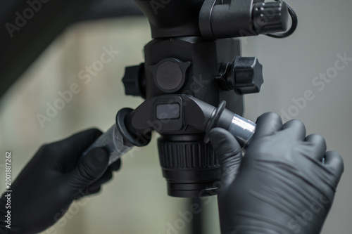 Close up of dentist hands in black gloves adjusting microscope