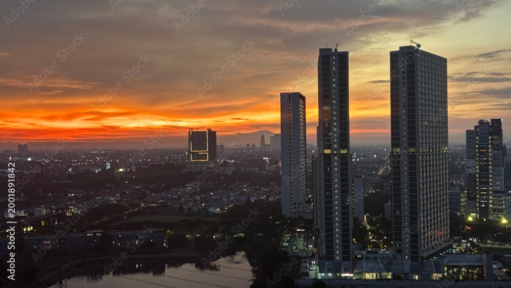 Fototapeta premium Dramatic golden sunset over a modern city skyline with tall skyscrapers and urban residential area.