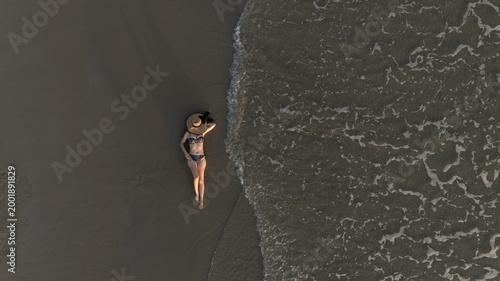 Fotografie Drone view of a woman in a black bikini relaxing happily on a sandy beach