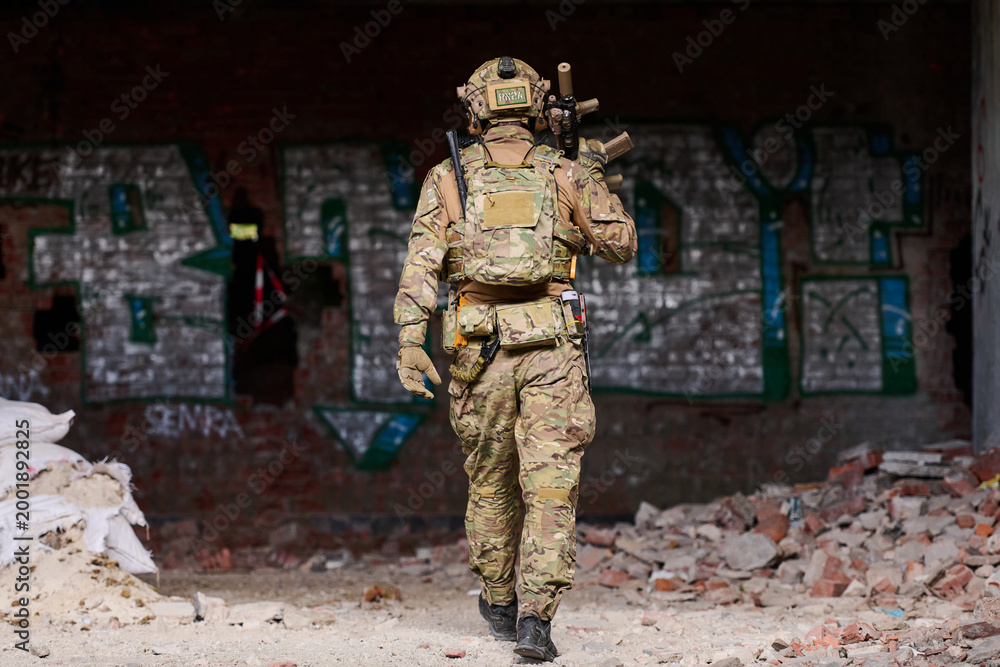 Fototapeta premium Soldier in Camouflage Tactical Gear Walking Through Abandoned Graffiti-Covered Building During Urban Military Training