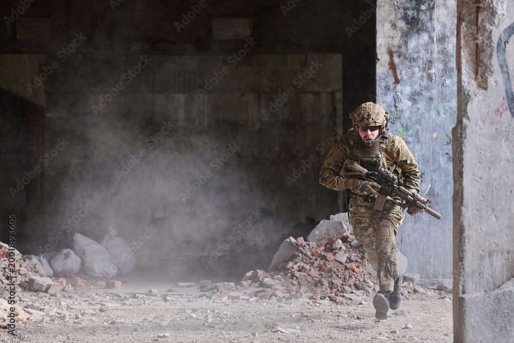 Obraz premium Armed Soldier In Camouflage Running Through Dusty Urban Ruins During Tactical Combat Training Operation