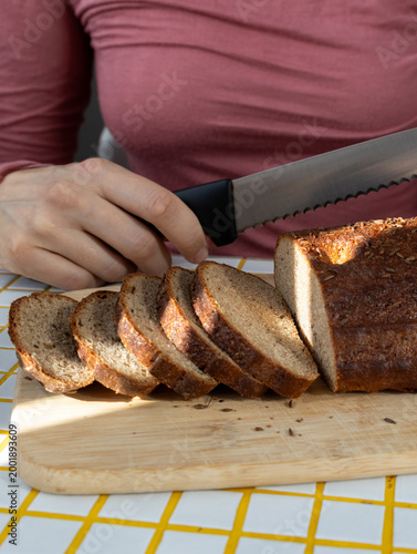 person cuts black bread on wooden board with knife. Sourdough rye bread with crispy crust. Bakery products. homemade cakes, yeast-free sourdough bread. Wholesome and healthy food. bakery.
