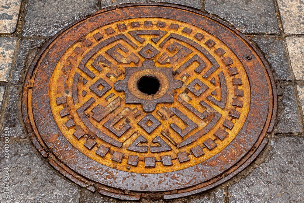 Obraz premium Rusty metal manhole cover with worn out geometric anti-slip patterns.