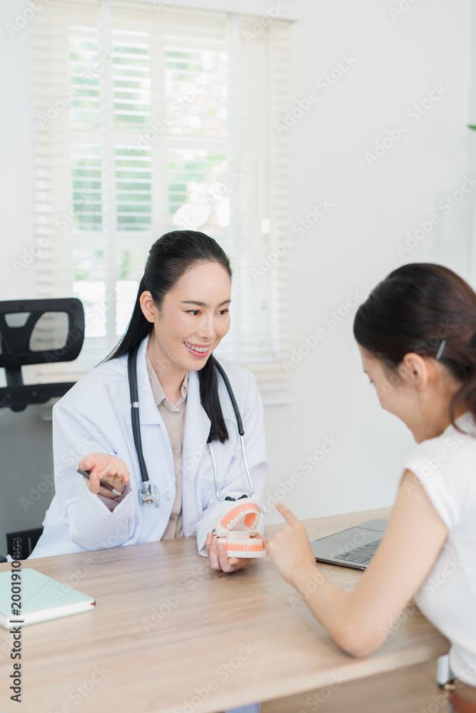 Obraz premium The dentist is talking to the patient and showing them a model of the teeth. (Concept of dental care)